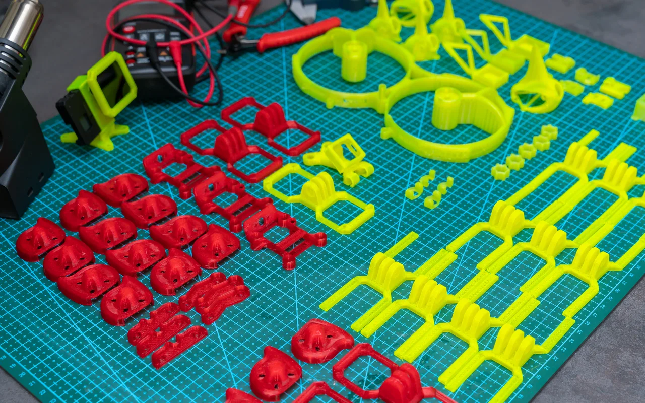 Dozens of red and yellow 3D printed parts laid out on a cutting mat