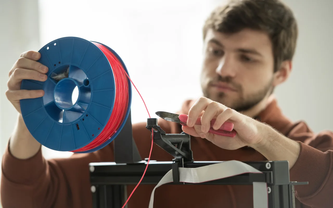 A maker holding a spool of red filament while trimming the end